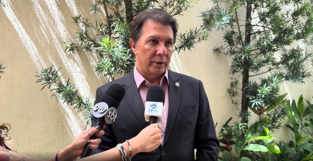 Deputado Arthur Maia, vice-presidente da FPPA, concedendo entrevista ao microfone de TV em ambiente externo com árvores e iluminação natural. Destaque para pauta de investimento em infraestrutura.