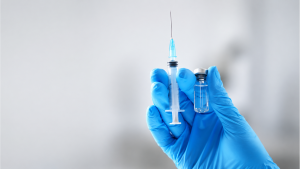Vacina Fluprevli: profissional de saúde em luvas azuis segurando seringa com agulha e frasco em ambiente clínico, simbolizando imunização contra influenza com registro na Anvisa.