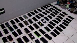 Grande quantidade de aparelhos celulares apreendidos pela Polícia Civil organizados sobre uma mesa durante a Operação Linha Segura na Baixada Santista.