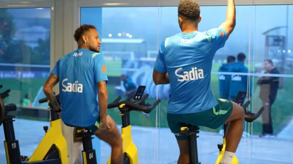 Neymar e Danilo sentados no banco de reservas acompanhando o treino da Seleção Brasileira na Granja Comary.