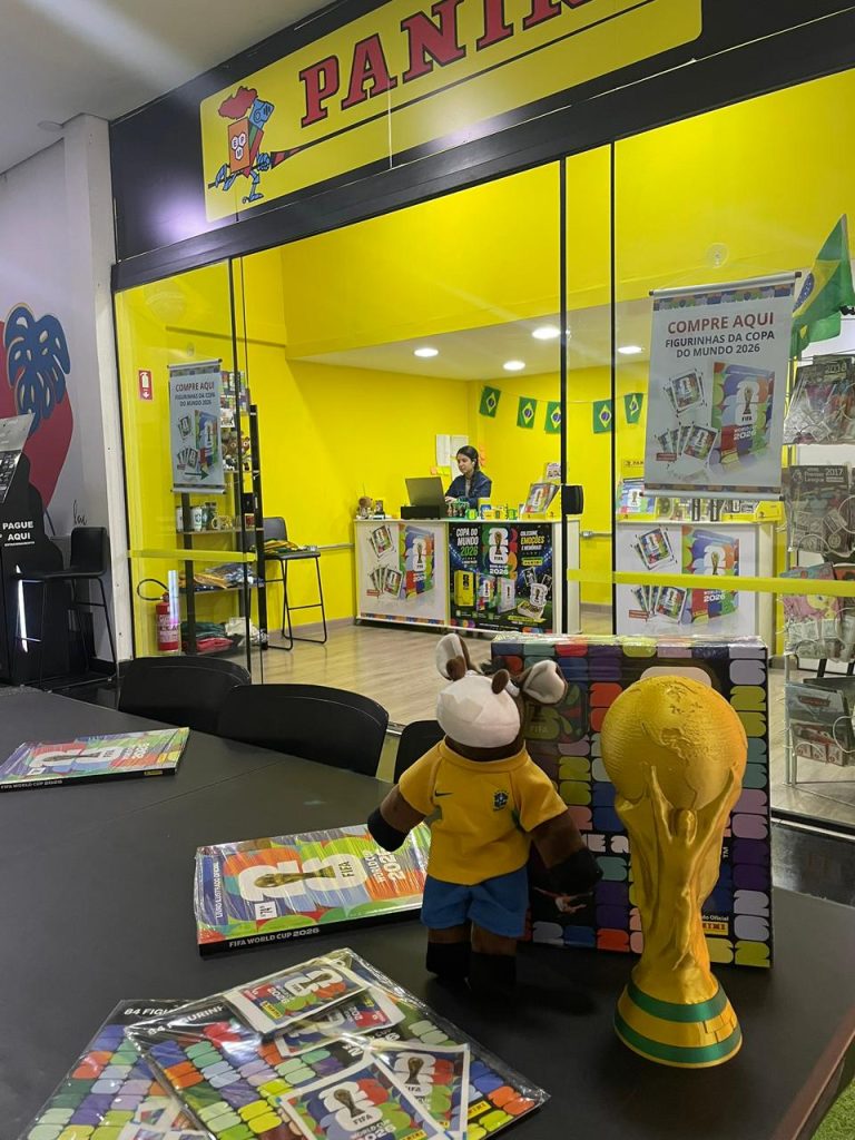 Espaço temático com mesas e cadeiras para colecionadores trocarem figurinhas da Copa de 2026 no corredor do Prado Boulevard Shopping.