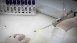 Profissional de saúde com vestimenta de proteção individual completa em ambiente laboratorial para análise de amostras do vírus Ebola.