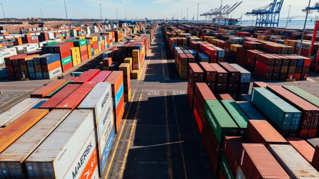 Pátio de logística com diversos contêineres coloridos empilhados, representando o fluxo de exportações brasileiras que podem ser impactadas pela nova sobretaxa de 25%.