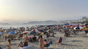 Vista panorâmica de uma praia na Baixada Santista com movimentação de turistas durante o feriado de Corpus Christi.