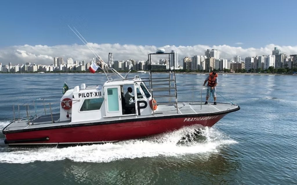 Lancha da Praticagem navegando próxima a um navio de grande porte para garantir a segurança operacional e ambiental em canal de acesso portuário.