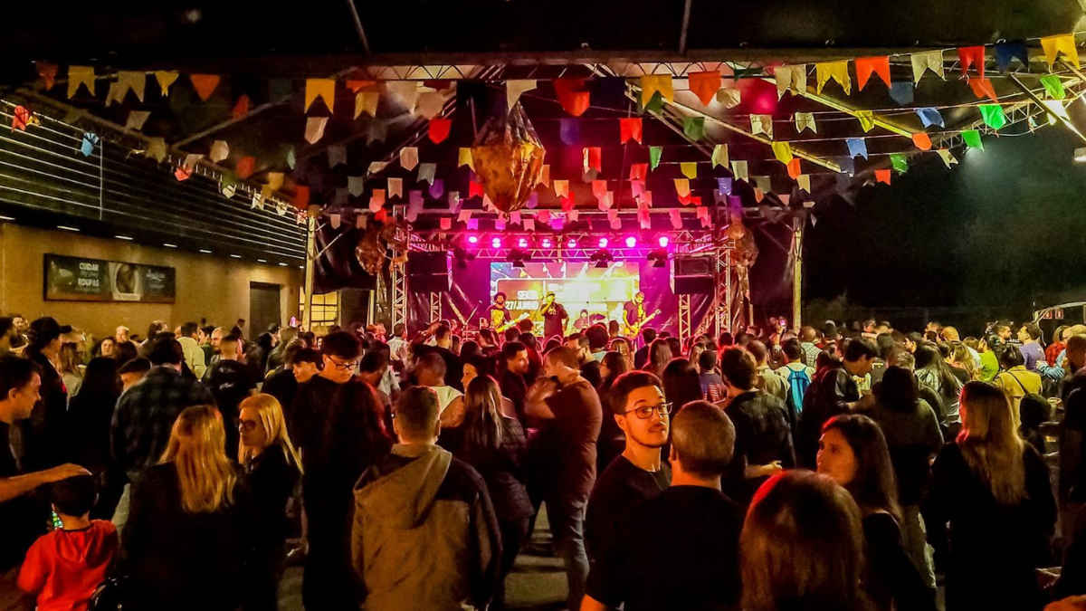 Público celebrando o Arraiá do Prado em Campinas com decoração de bandeirinhas e barracas de comidas típicas em ambiente ao ar livre.