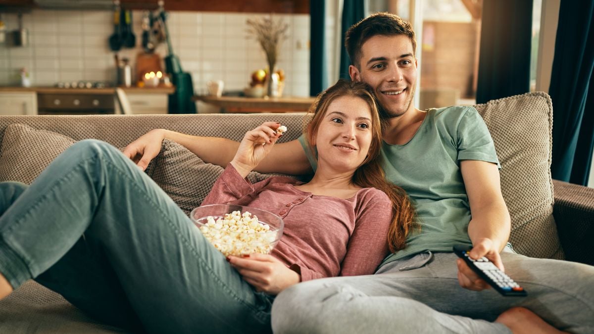 Casal abraçado no sofá assistindo a um filme romântico na televisão, representando uma noite de cinema em casa para o Dia dos Namorados.