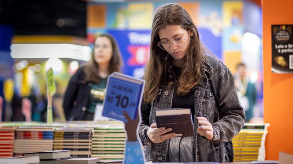 Visitante lendo livro em área de convivência da Bienal do Livro de SP, simbolizando a experiência cultural e o incentivo à leitura do evento.