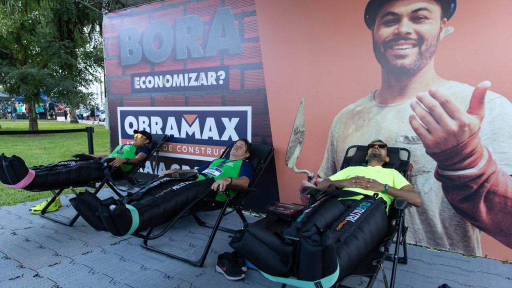 Corredores utilizando botas de compressão pneumática para recuperação muscular no estande da Obramax após a Meia de Santos.