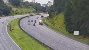 Trânsito lento na Rodovia Anchieta–Imigrantes, com filas de veículos em trecho cercado por áreas verdes e placas de sinalização, em quinta-feira (25).