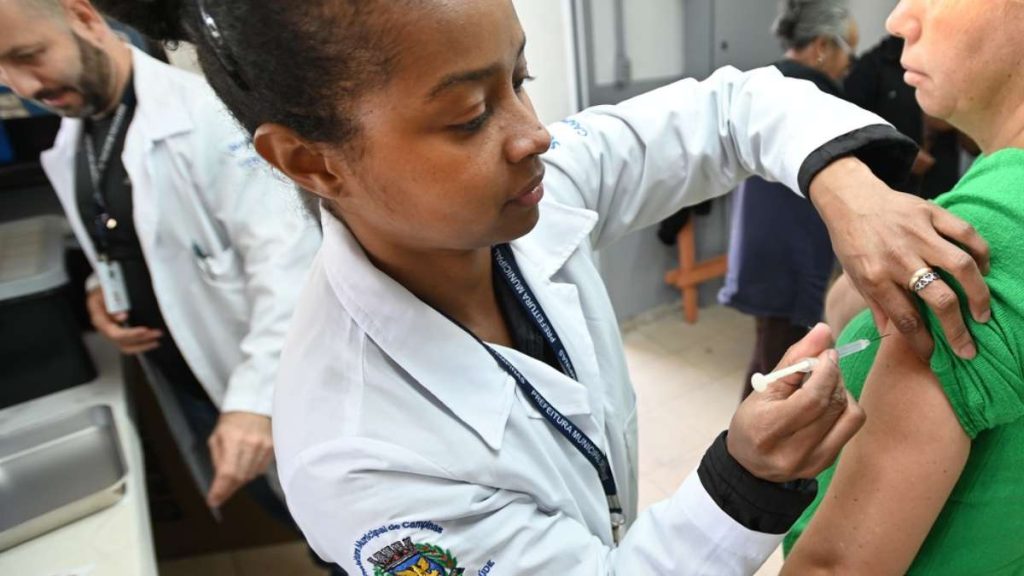 Profissional de saúde aplica vacina no braço de um paciente em ambiente hospitalar, destacando a morte por gripe Campinas e o aumento de óbitos registrados na cidade.