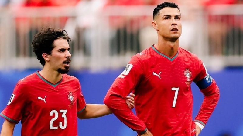 Cristiano Ronaldo em campo com camisa da seleção de Portugal, enquanto um jogador da RD Congo reage após o empate em partida amistosa ou eliminatória.