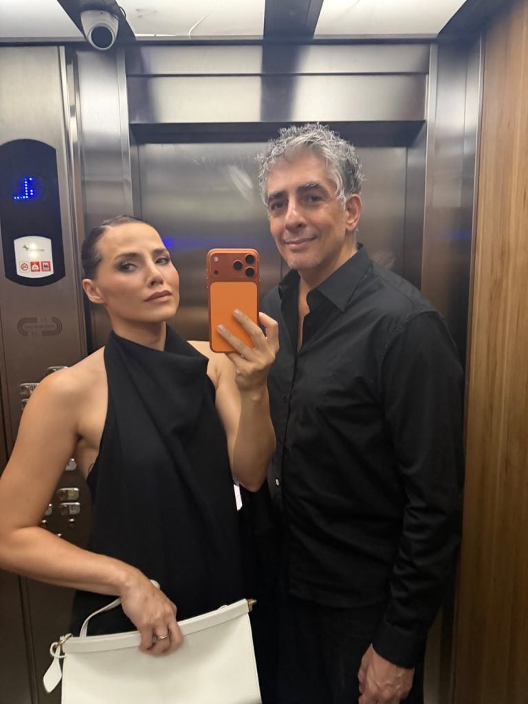 Leticia Colin e seu par aparecem em um corredor, vestindo roupas pretas e posando para uma foto com celular, após a reconciliação e vivendo em casas separadas.