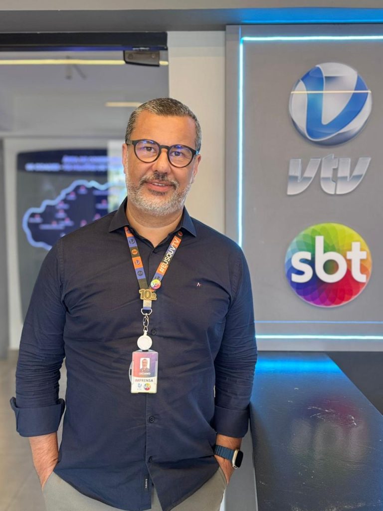 Luciano Pessoa, gerente comercial da VTV Copa Sabesp, em evento ao lado de um painel com logo VTV, esfera azul e identificação SBT.