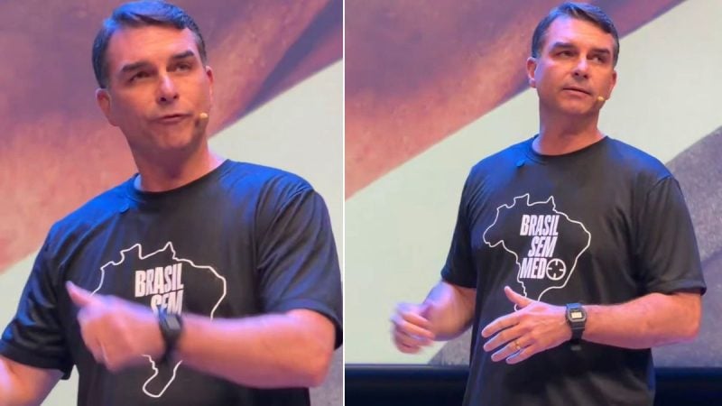 Flávio Bolsonaro aparece em vídeo em um palco, usando camiseta escura com a estampa “Brasil sem medo”, fazendo gestos com as mãos durante uma apresentação ou entrevista.