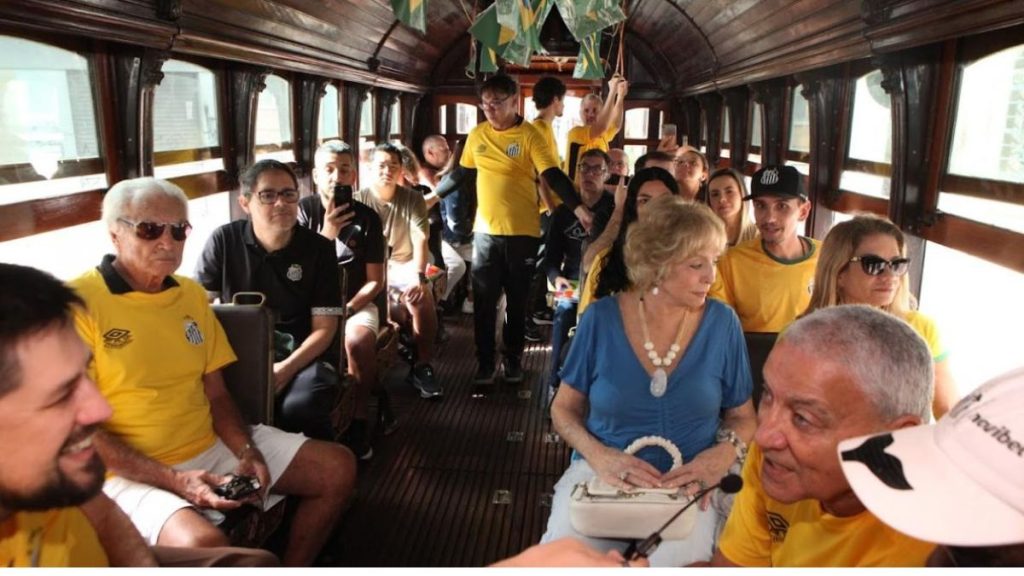 Bonde da Copa: grupo de passageiros em passeio temático dentro de um vagão decorado, com clima de nostalgia e história, enquanto aproveitam a experiência em Santos.
