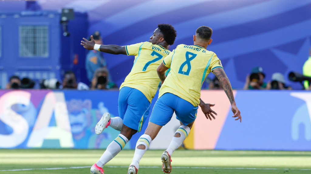 Vini Jr. comemora um gol contra Marrocos durante o jogo do Brasil, em uma partida de futebol com jogadores em campo e bandeiras ao fundo