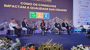 Conexidades: painel com especialistas em palco durante evento sobre como os conselhos impactam a qualidade das cidades, com fundo montanhas e banners institucionais