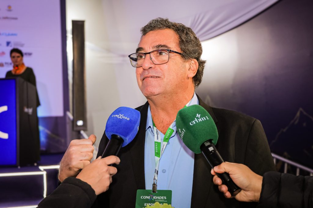 Dr. Edgar Garcez Junior, presidente do Conselho Federal de Biomedicina, concedendo entrevista em evento com microfones e crachá, destacando Conexidades e comunicação institucional.