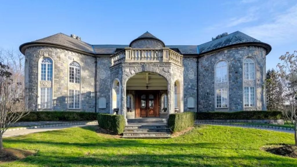 Vista externa de um castelo com fachada azul e janelas amplas, entrada central e jardim bem cuidado ao redor, em cenário residencial nos EUA