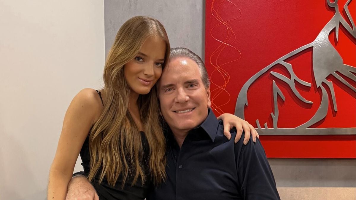 Rafa Justus ao lado de Roberto Justus em foto sorridente, com parede clara ao fundo e painel vermelho decorado, em momento de recepção especial durante a mudança para a casa de Roberto Justus.