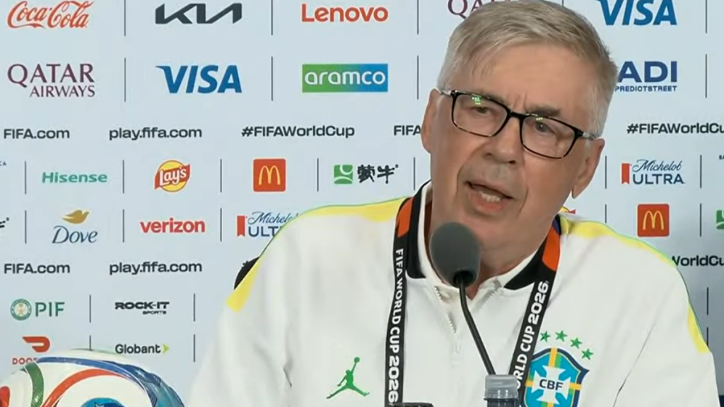 Carlo Ancelotti aparece em coletiva de imprensa, ao lado de credencial e microfone, em cenário com patrocinadores e marca da FIFA, liderando o ranking dos Técnicos mais bem pagos da Copa do Mundo 2026.
