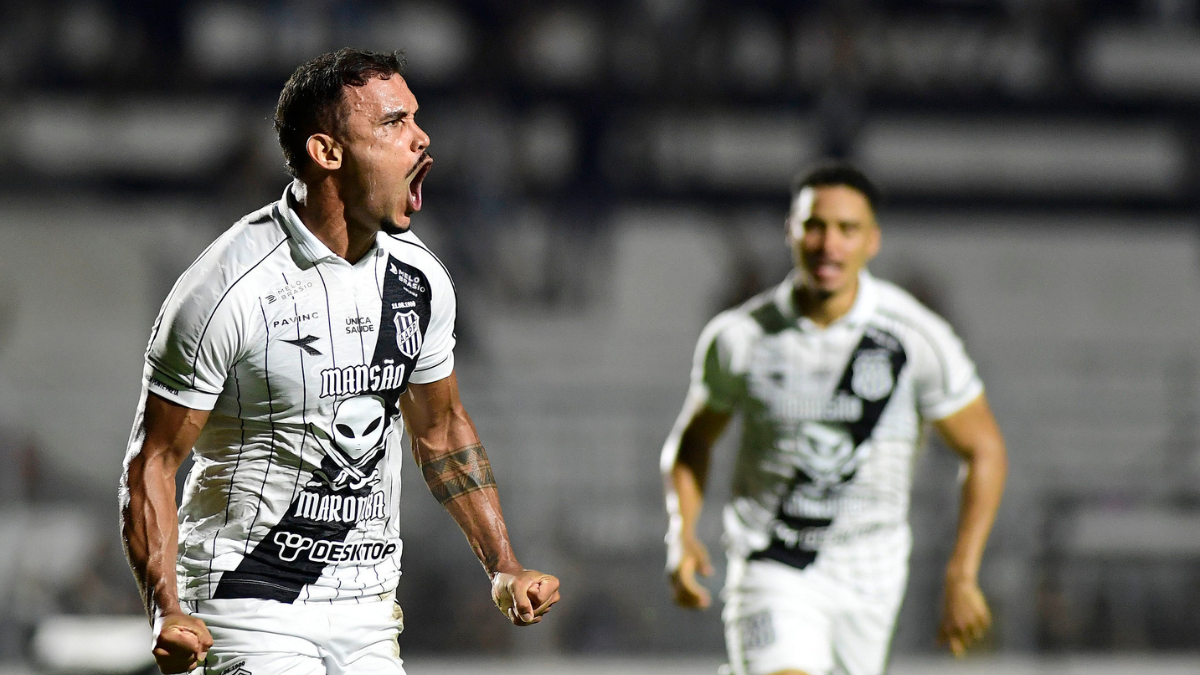 Willian Pottker Ponte Preta em campo durante jogo, com expressão intensa e braços abertos, enquanto jogador do clube aparece desfocado ao fundo