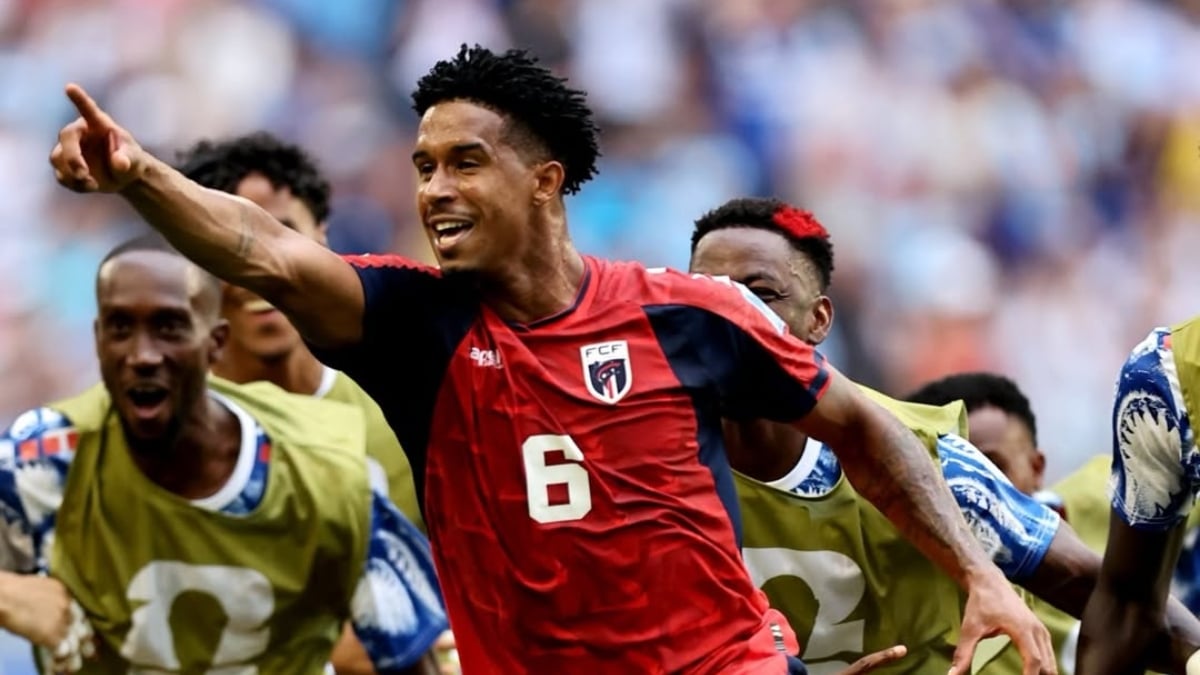 Jogador da seleção de Cabo Verde em partida de futebol, com a camisa vermelha e número 6, comemorando ao lado de companheiros em um estádio lotado, pela classificação.