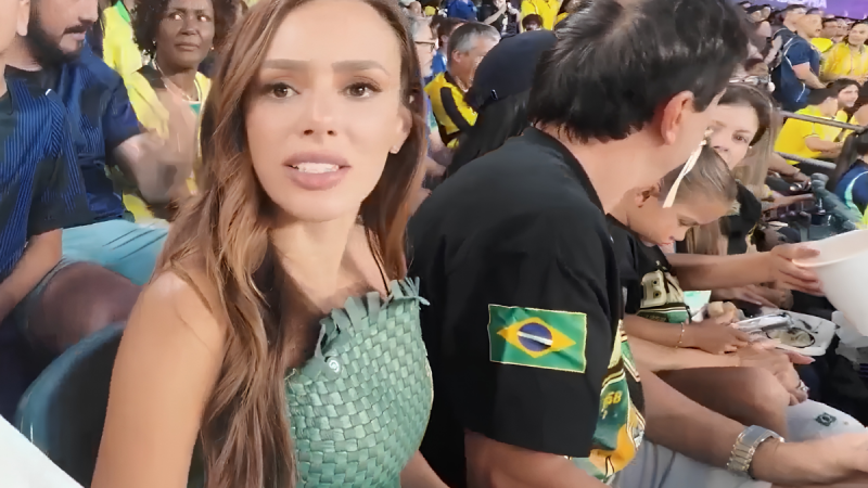 Bruna Biancardi aparece em registro no estádio, ao lado de pessoas na plateia. Ela está em primeiro plano, usando vestido verde e segurando um olhar para a câmera, em um contexto de evento esportivo.