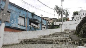 Cenário urbano em área de morro no litoral de São Paulo, com casas simples e escadaria de concreto, em registro de patrulhamento relacionado a PM baleado morro Santos.