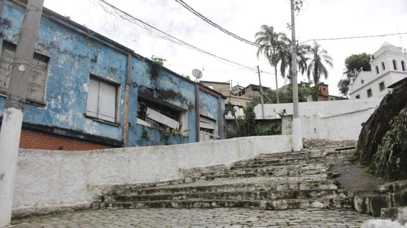 Cenário urbano em área de morro no litoral de São Paulo, com casas simples e escadaria de concreto, em registro de patrulhamento relacionado a PM baleado morro Santos.