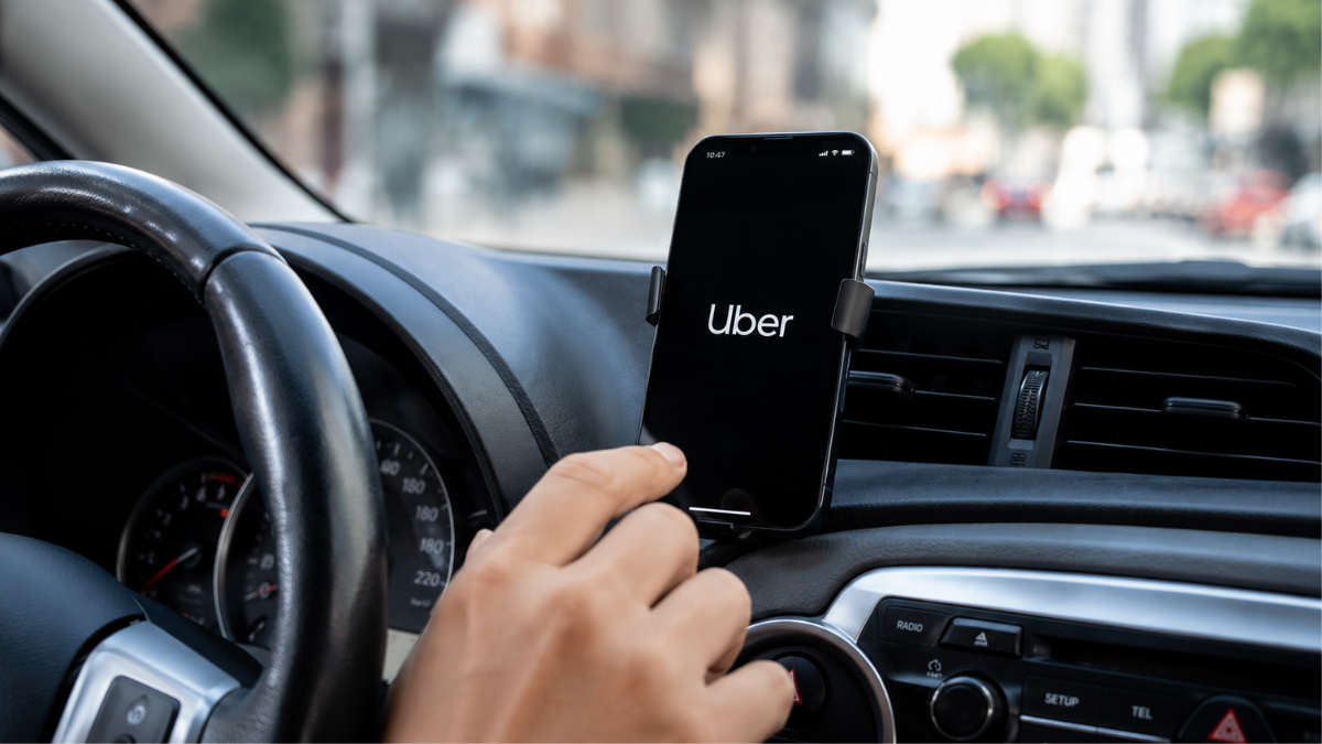Motorista segura o celular com o aplicativo Uber em um carro durante uma corrida, com o suporte do smartphone no painel. Uber remove modelos das categorias Uber Black e Comfort.