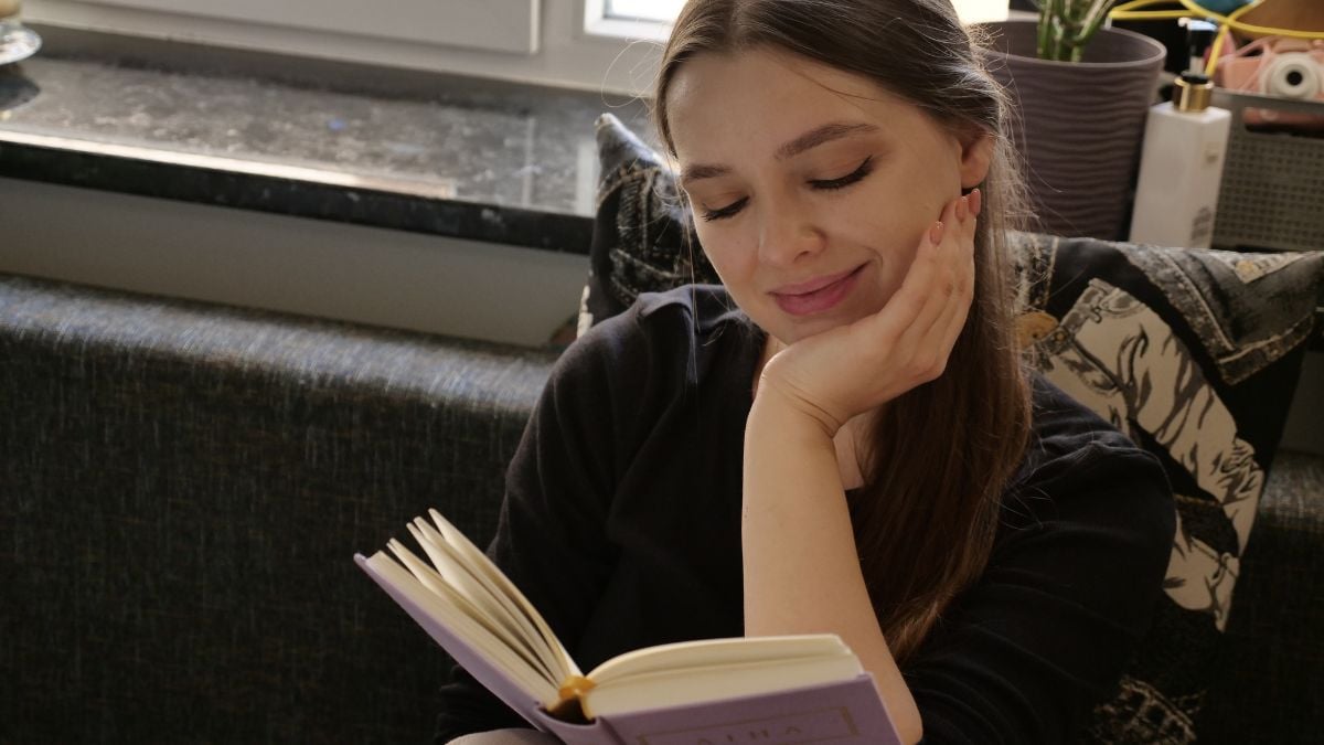 Mulher lendo um livro aberto no sofá, em ambiente aconchegante, com clima de mistério e romances para lançamentos de livros Julho 2026.