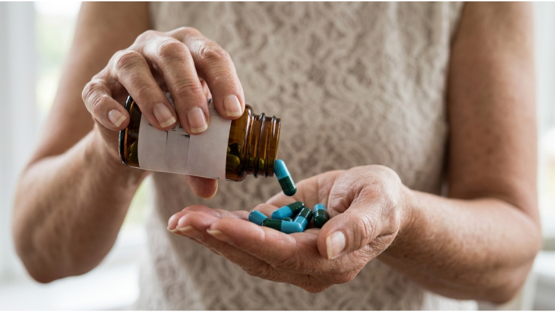 Mulher idosa segurando um frasco de comprimidos e cápsulas em sua mão, com medicamento não hormonal para controle dos sintomas da menopausa após liberação da Anvisa.