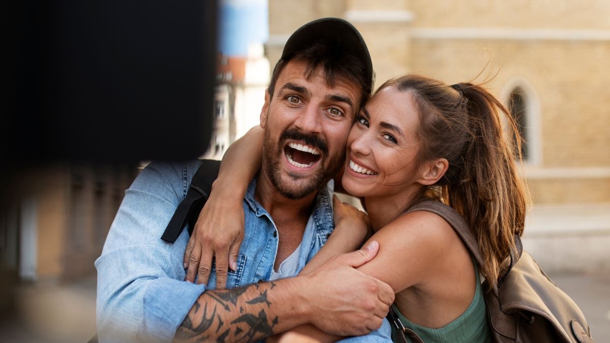 Amizade colorida: casal de amigos sorri e abraça em clima de cumplicidade ao ar livre, com expressão alegre e conexão emocional no dia a dia.