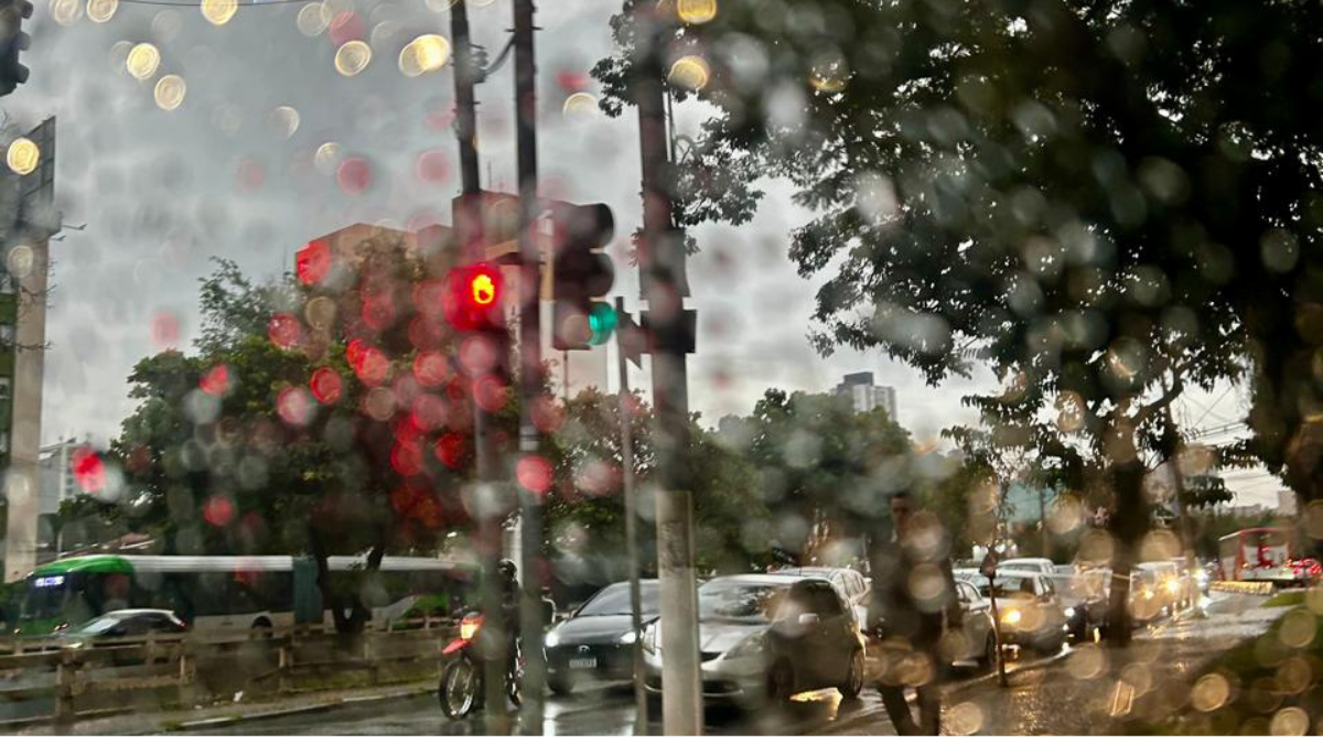 Chuva intensa em São Paulo, com gotas na lente e semáforos ao fundo, ruas alagadas e carros em movimento; cenário de alerta da Defesa Civil por chuvas em SP.