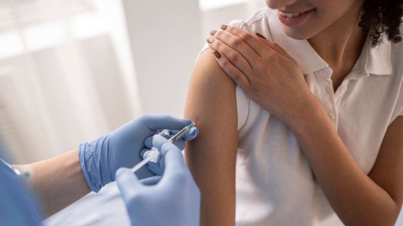 Profissional de saúde aplica vacina de gripe na parte superior do braço, com seringa e luvas, enquanto a pessoa posiciona o braço para imunização. Vacinação contra gripe em Americana neste sábado.
