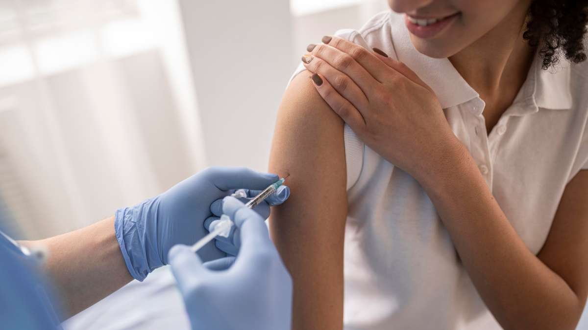 Profissional de saúde aplica vacina de gripe na parte superior do braço, com seringa e luvas, enquanto a pessoa posiciona o braço para imunização. Vacinação contra gripe em Americana neste sábado.