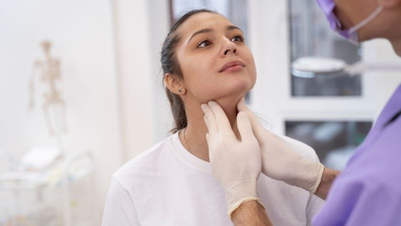 Médico examina paciente em clínica, com a mão apoiada na região do pescoço, sugerindo avaliação de sinais do câncer de cabeça e pescoço.