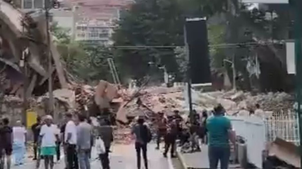 Terremoto na Venezuela: ruas com escombros e multidão se deslocando após a destruição, com pessoas e estruturas danificadas ao fundo.