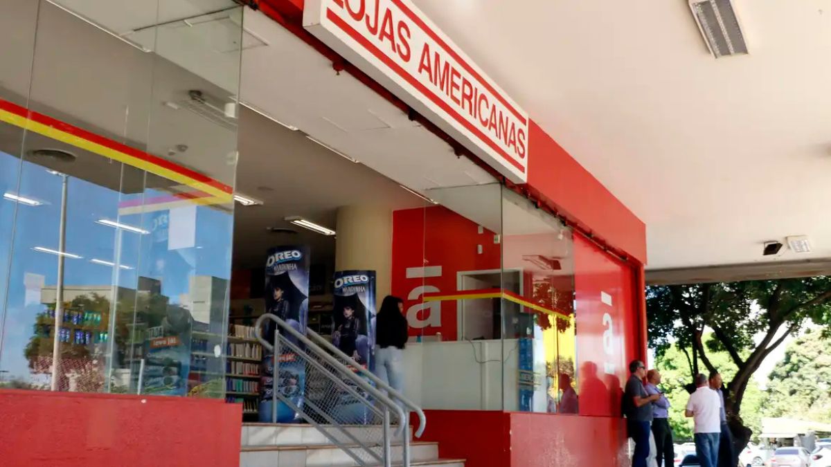Fachada de loja da Americanas com faixa vermelha e letreiro “Lojas Americanas”, entrada com escada e pessoas em frente, em imagem relacionada ao caso Americanas.