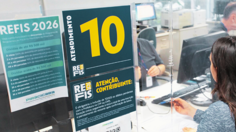 Campanha de Refis Piracicaba em atendimento: cartazes com descontos e regra de renegociação de dívidas, enquanto um atendente e uma cliente trabalham em computadores no escritório.