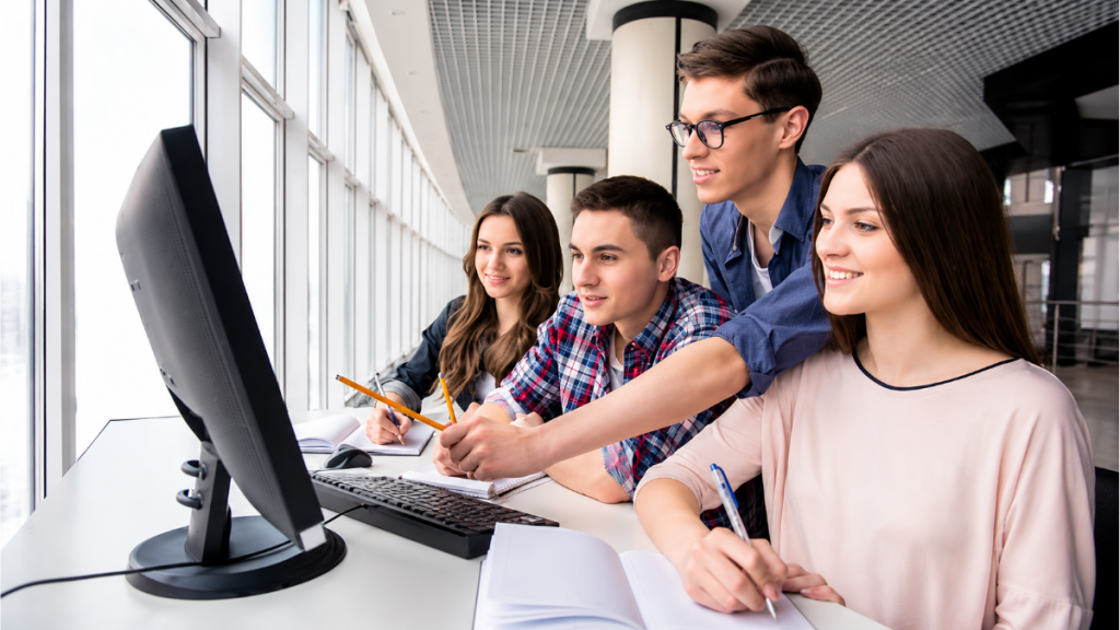 Jovens estudantes trabalhando em frente a um computador em um ambiente de escritório, com cadernos e canetas, ilustrando oportunidades de vagas de estágio em Valinhos com bolsa-auxílio de até R$ 2.061.