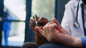 Médico aplica exame de saúde em uma mão com aparelho, em ambiente clínico, destacando ações gratuitas de prevenção ao diabetes nas policlínicas de Santos.