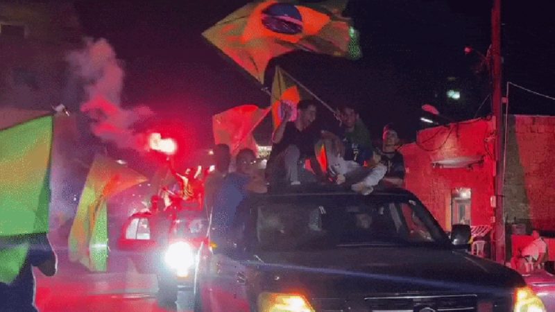 Libaneses comemorando vitória do Brasil em noite de festa, com carro lotado de pessoas, bandeiras e sinalizadores vermelhos e fumaça ao fundo.