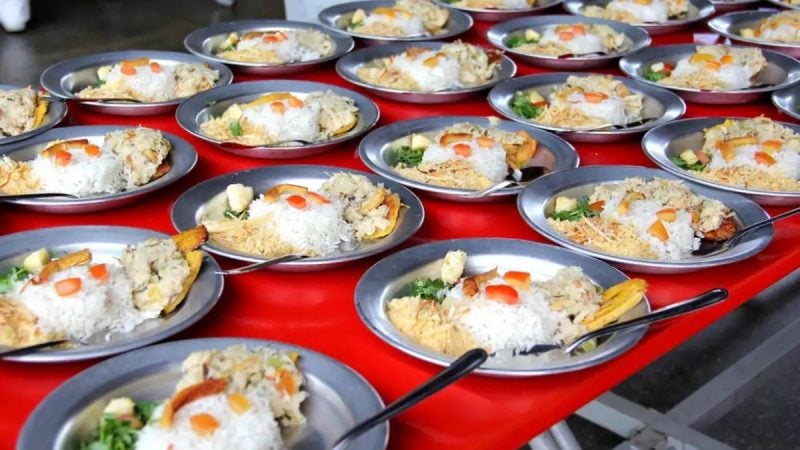 Pratos de almoço servidos em bandejas vermelhas, com arroz branco e acompanhamentos, evidenciando a oferta de alimentação escolar em escolas estaduais de SP durante o período de férias.