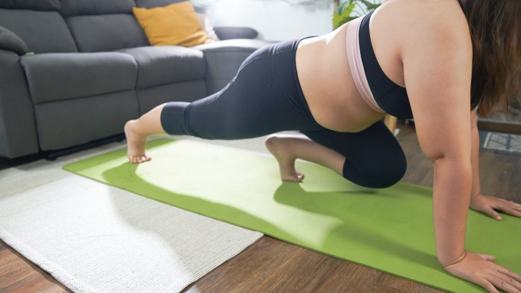Pessoa realizando prancha em cima de um colchonete verde no sala de estar, com treino de exercícios físicos; imagem usada para contextualizar discussão sobre canetas emagrecedoras e perda de peso.