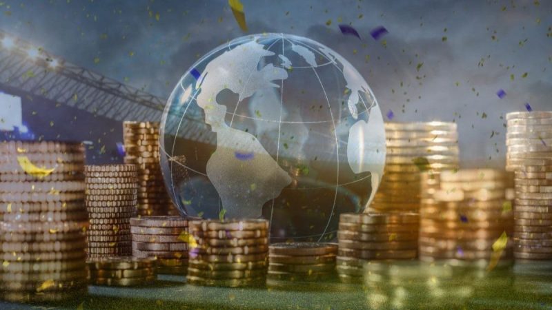 Ilustração de um globo terrestre sobre pilhas de moedas, remetendo a pagamentos e ao fluxo financeiro entre Brasil e Japão. Visual relacionado ao atendimento bancário hoje nesta segunda-feira.