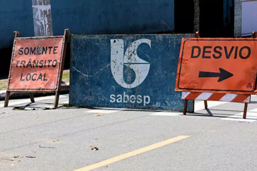 Placas de sinalização de trânsito com inscrições “Somente trânsito local” e “Desvio” em via pública, com fundo azul da SABESP, indicando obras de água e esgoto na Baixada Santista (Praia Grande, Itanhaém e Peruíbe).