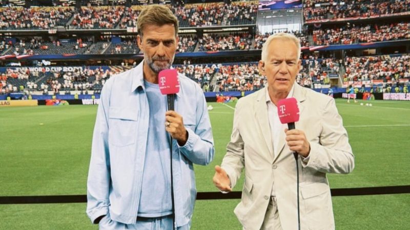 Klopp aparece em um estádio durante transmissão esportiva, com microfone nas mãos, ao lado de outro apresentador; a cena remete a críticas após eliminação da Alemanha para o Paraguai.